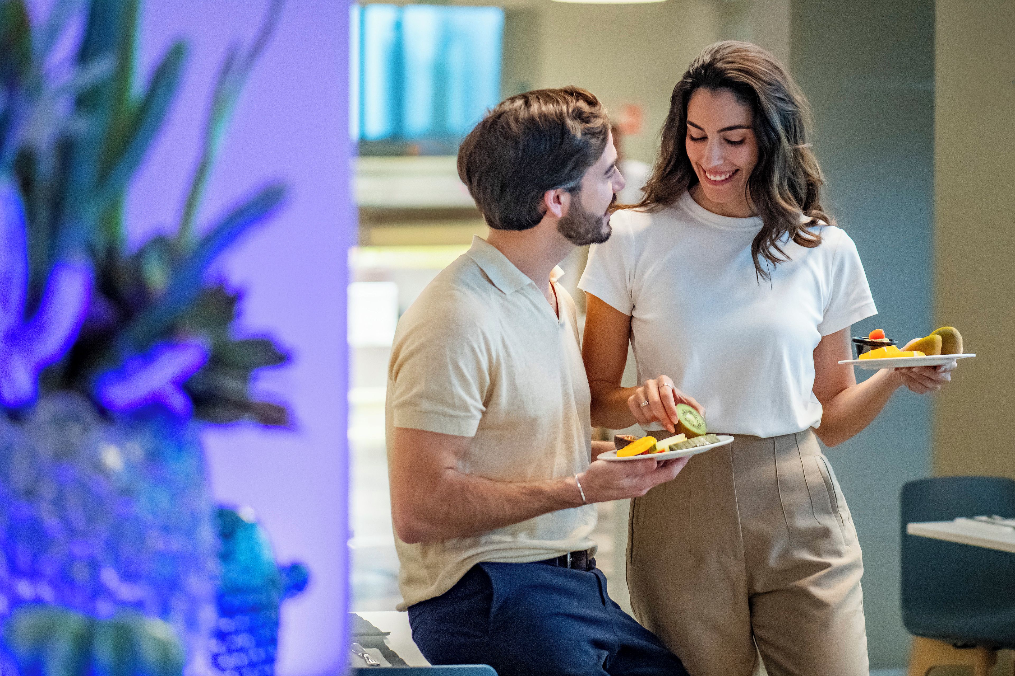 Two people dining indoors, one holding a plate with food.
