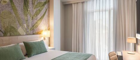 A hotel room with a bed, a desk, a chair, a TV, and a large window with curtains.