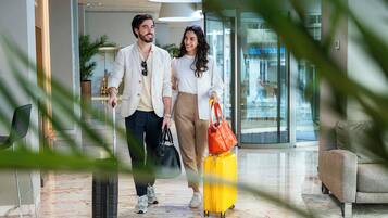 A man and a woman walking with luggage in a modern lobby with marble flooring and a seating area.