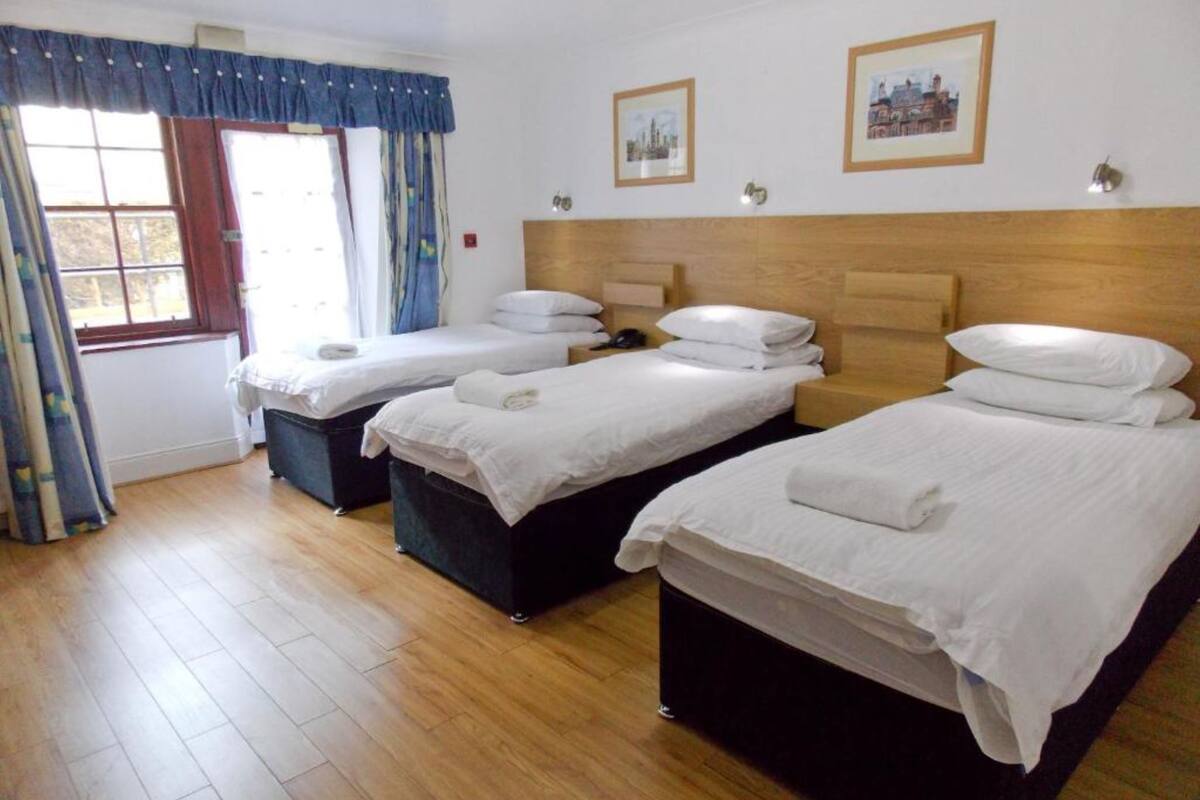 A hotel room with three single beds, wooden headboards, and a large window with curtains.