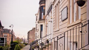 A narrow street with stone steps leading to a building with a black iron railing. - The Victorian House (Glasgow)