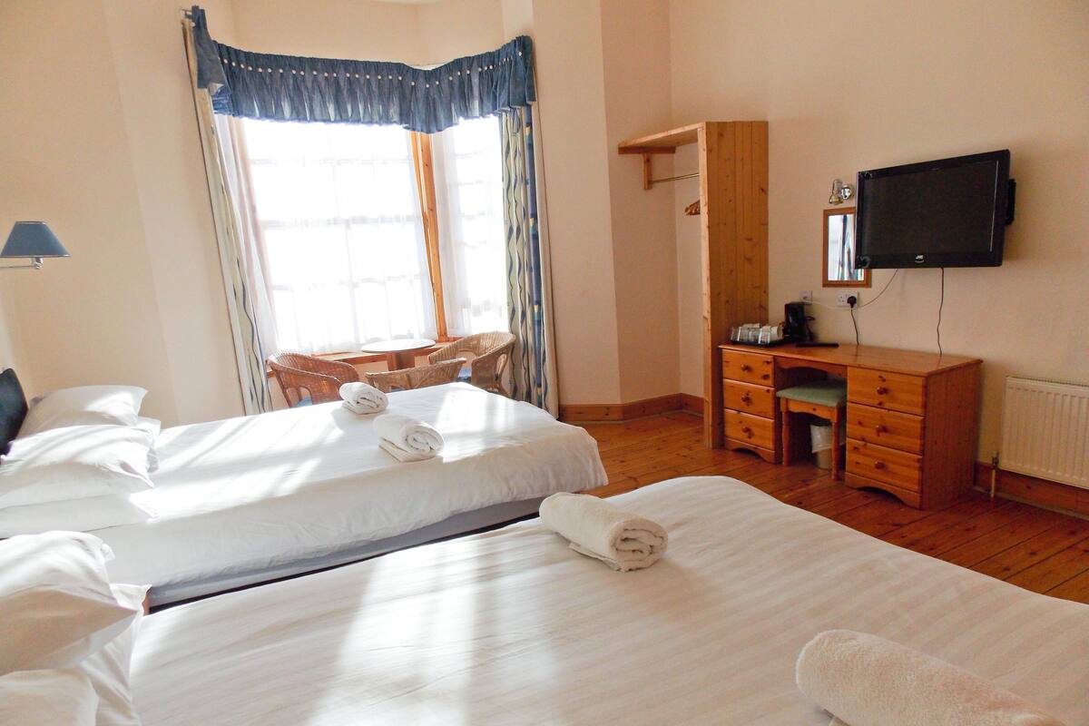 A hotel room with two beds, a desk, a chair, and a TV.