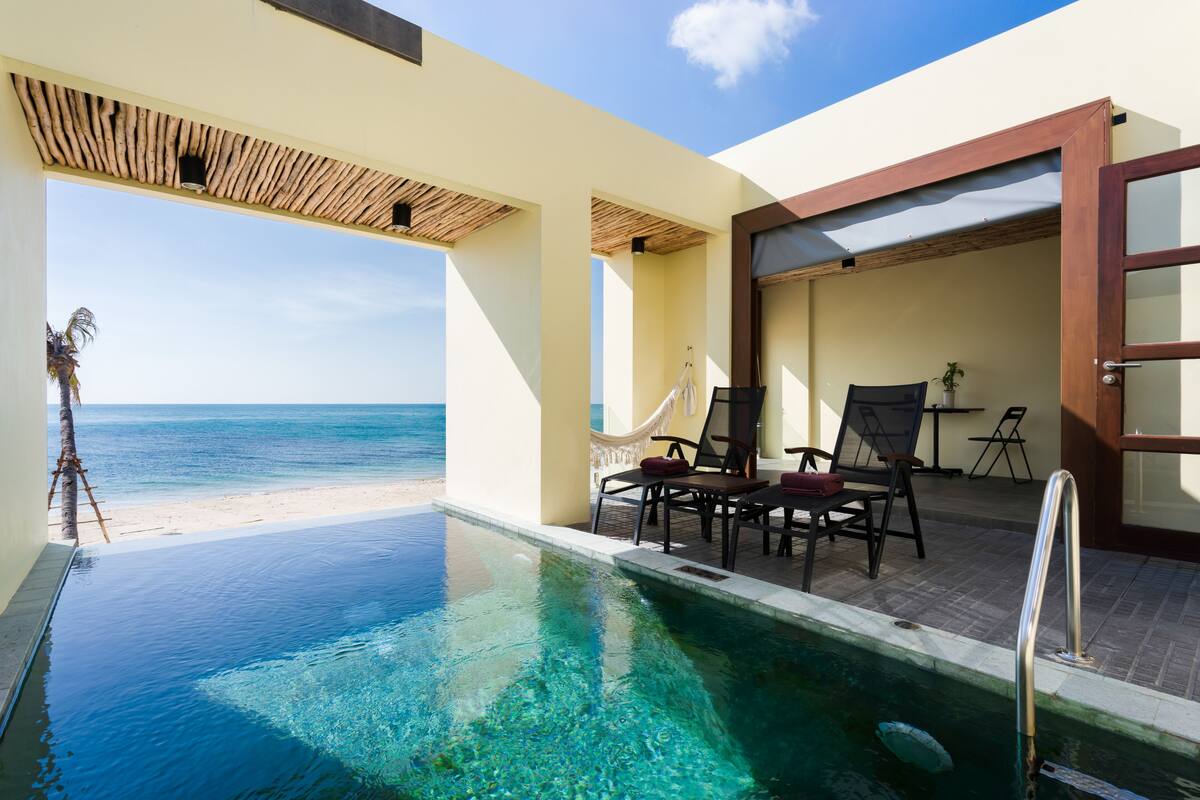 A pool area with clear water, a hammock, and a view of the ocean.