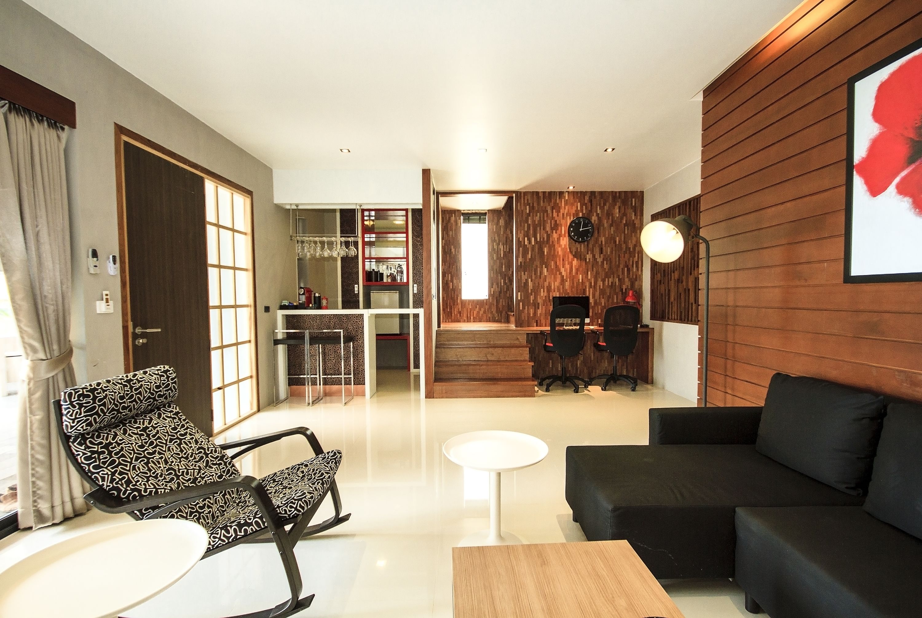 A modern living room with a black sofa, patterned chairs, a small white table, and a wooden accent wall.
