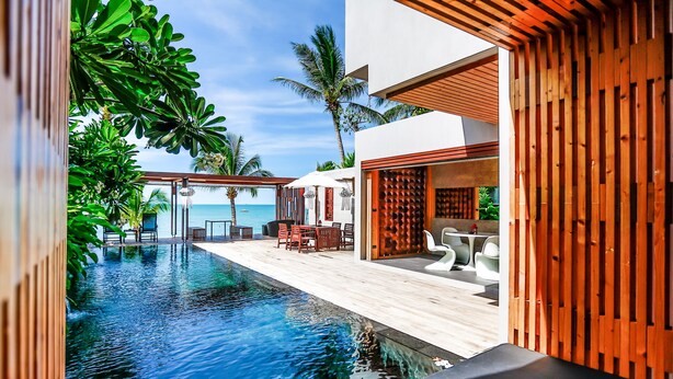 A modern pool area with a wooden deck, lounge chairs, and a view of the ocean.
