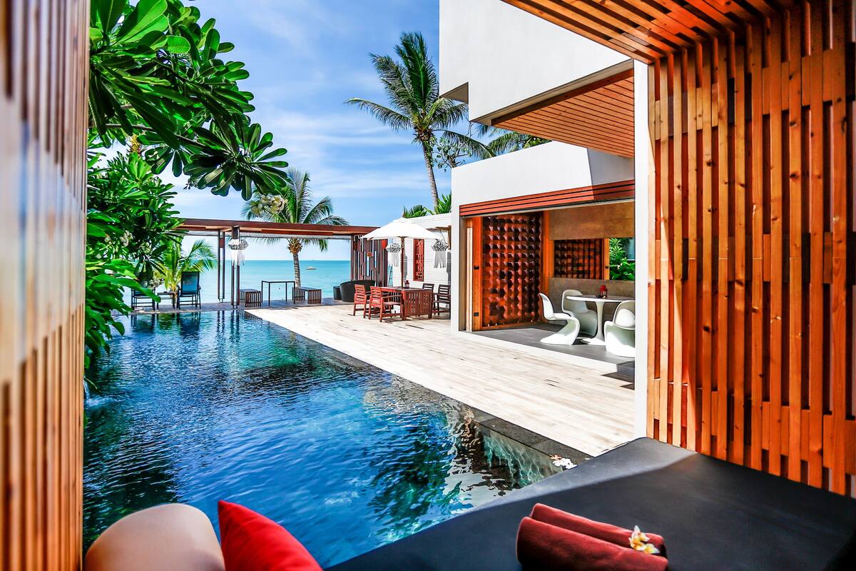 A modern pool area with a wooden deck, lounge chairs, and a view of the ocean.