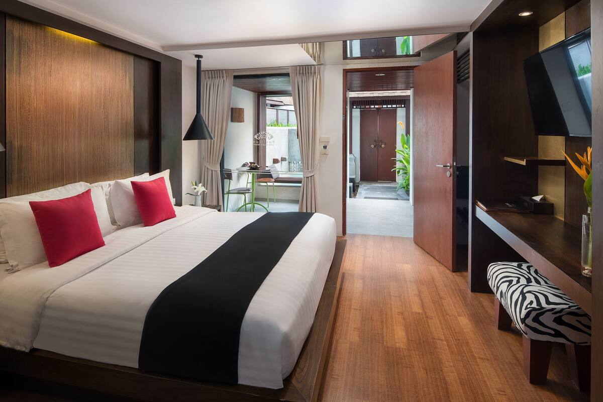 A modern hotel room with a large bed, a desk, a television, and a bench.