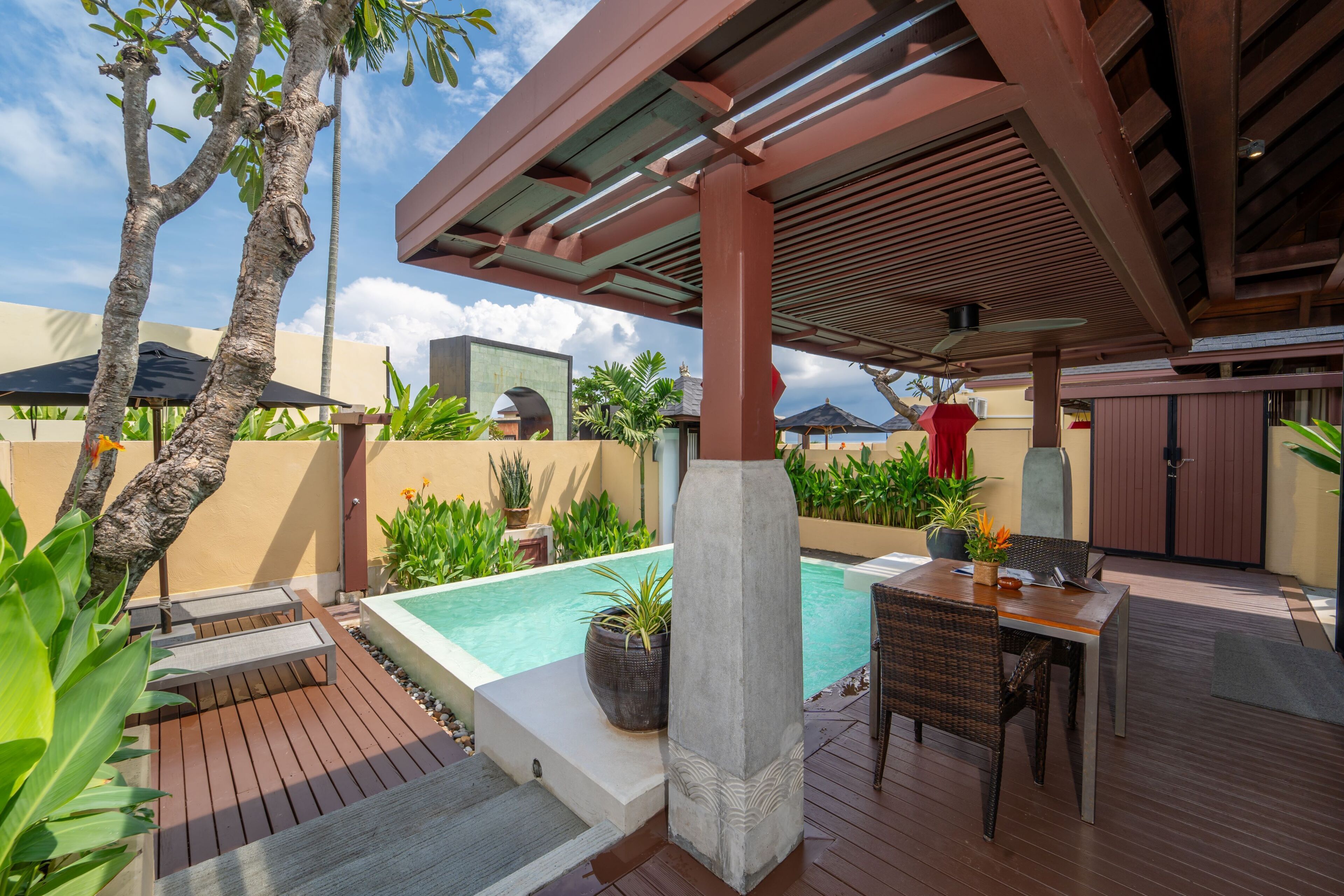 A poolside area with a wooden deck, a concrete column, and a covered seating area.
