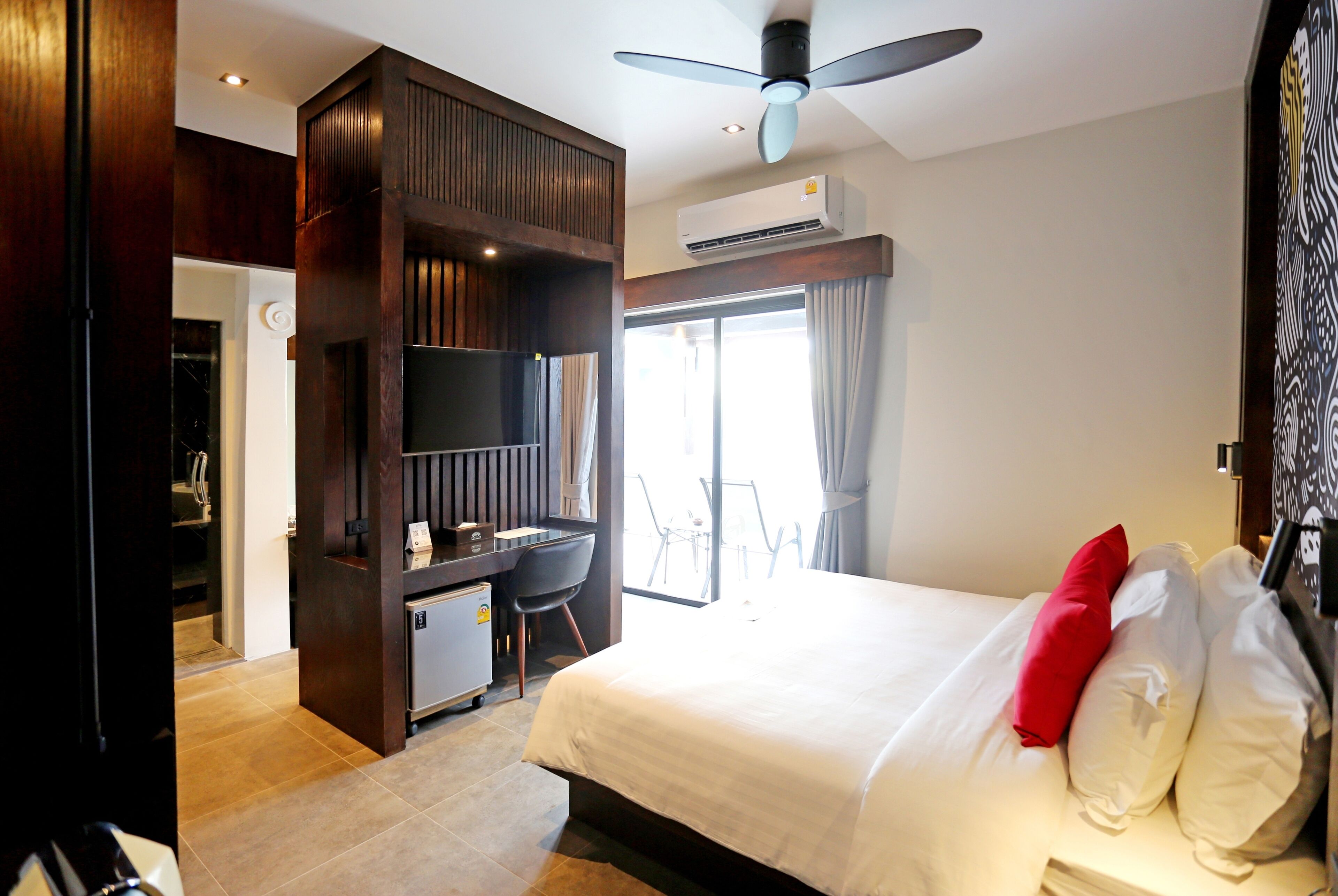 A hotel room with a bed, a desk, a chair, a ceiling fan, and an air conditioning unit.