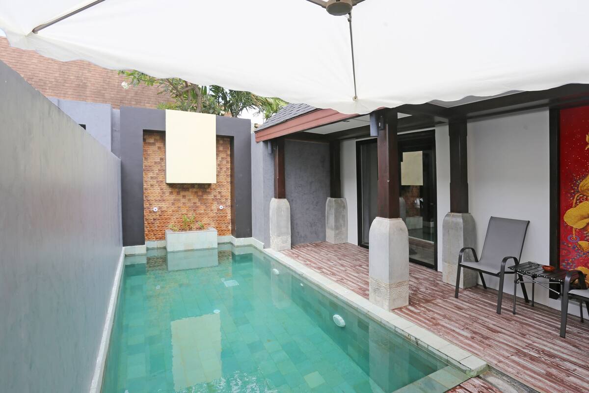 A swimming pool with a tiled deck, a covered seating area, and a brick wall.