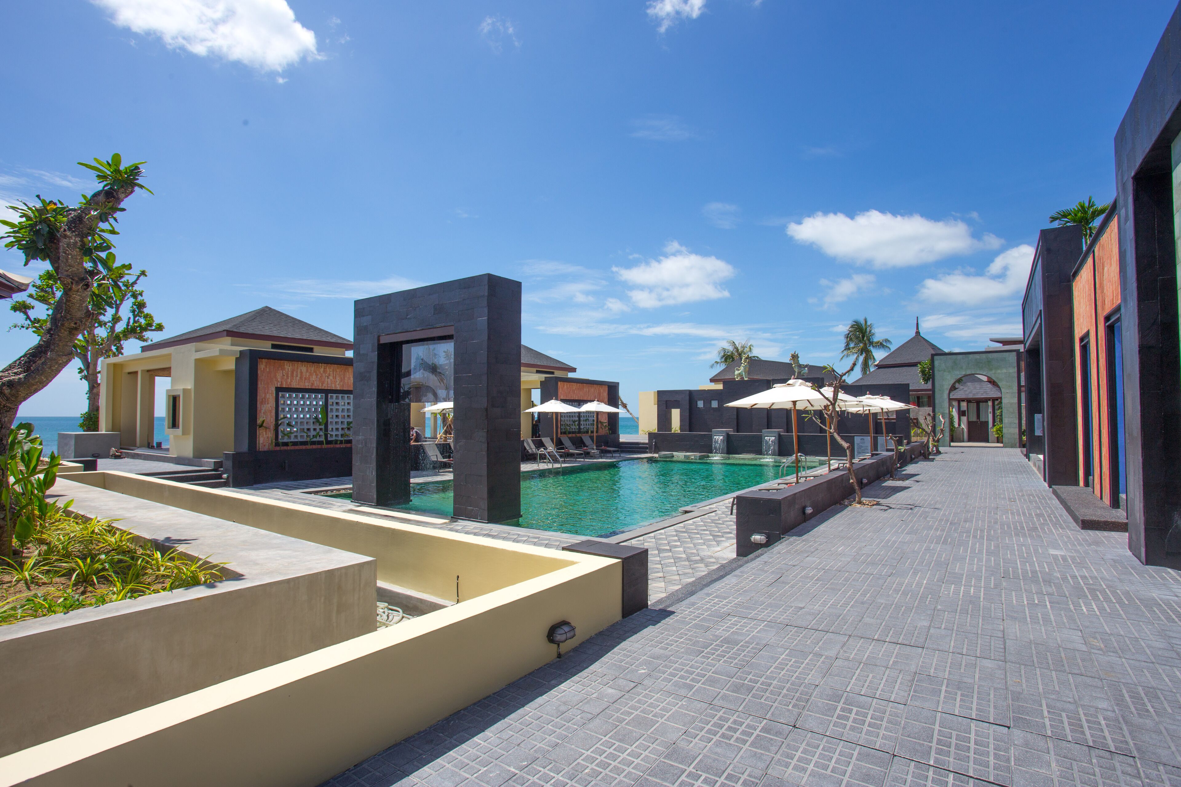 A poolside area with lounge chairs and umbrellas, a clear blue sky, and a view of the sea.