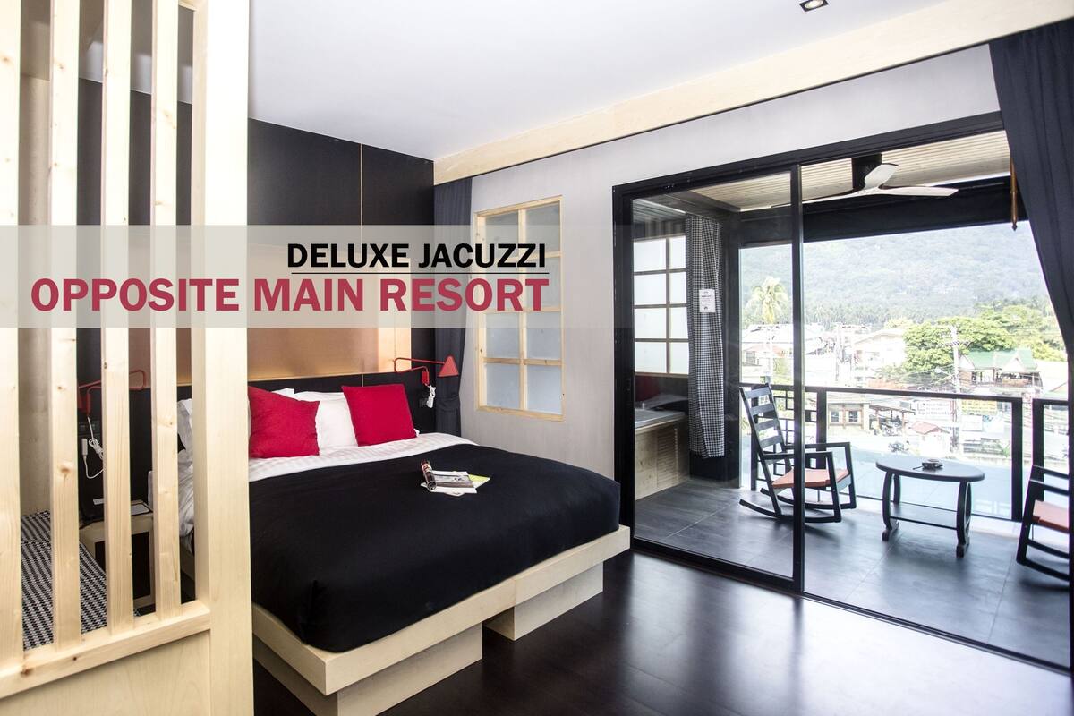 A Deluxe Jacuzzi room with a bed, a balcony with a view, and a large window.