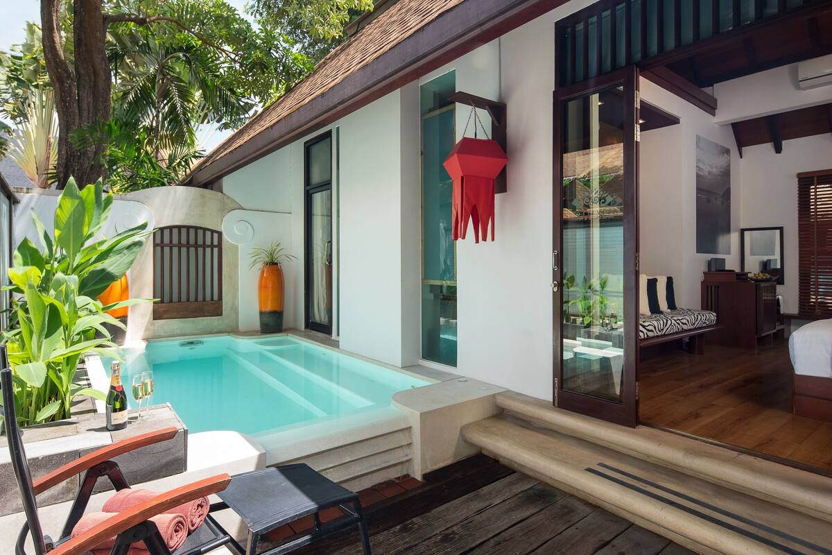 A modern pool area with a glass-enclosed room, a wooden deck, and a seating area with a table and chairs.