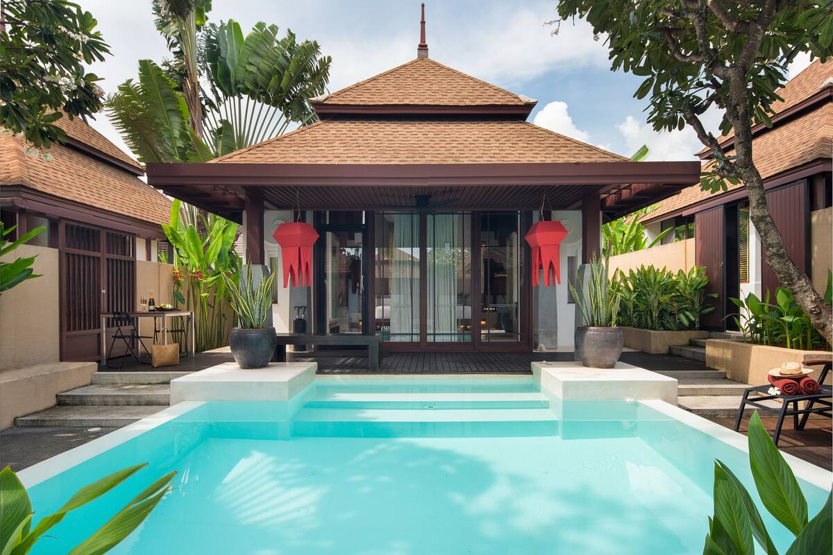 A swimming pool with a covered area, surrounded by lush greenery and a traditional building with a tiled roof.