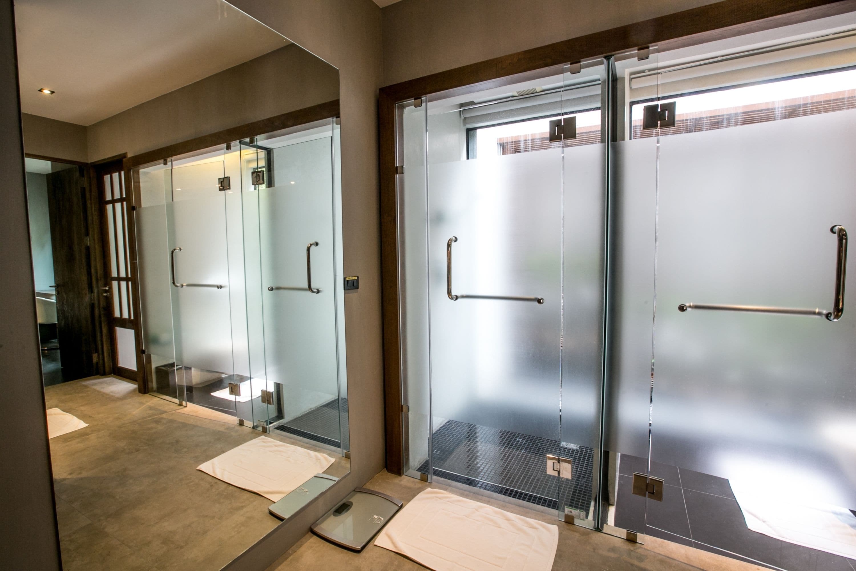 Un baño de hotel moderno con puertas de ducha de vidrio, una balanza y un perchero para toallas.