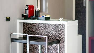 A modern kitchenette with a coffee machine, a patterned backsplash, and a glass-top table.