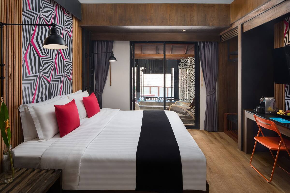 A hotel room with a large bed, a desk, and a view of the outside.