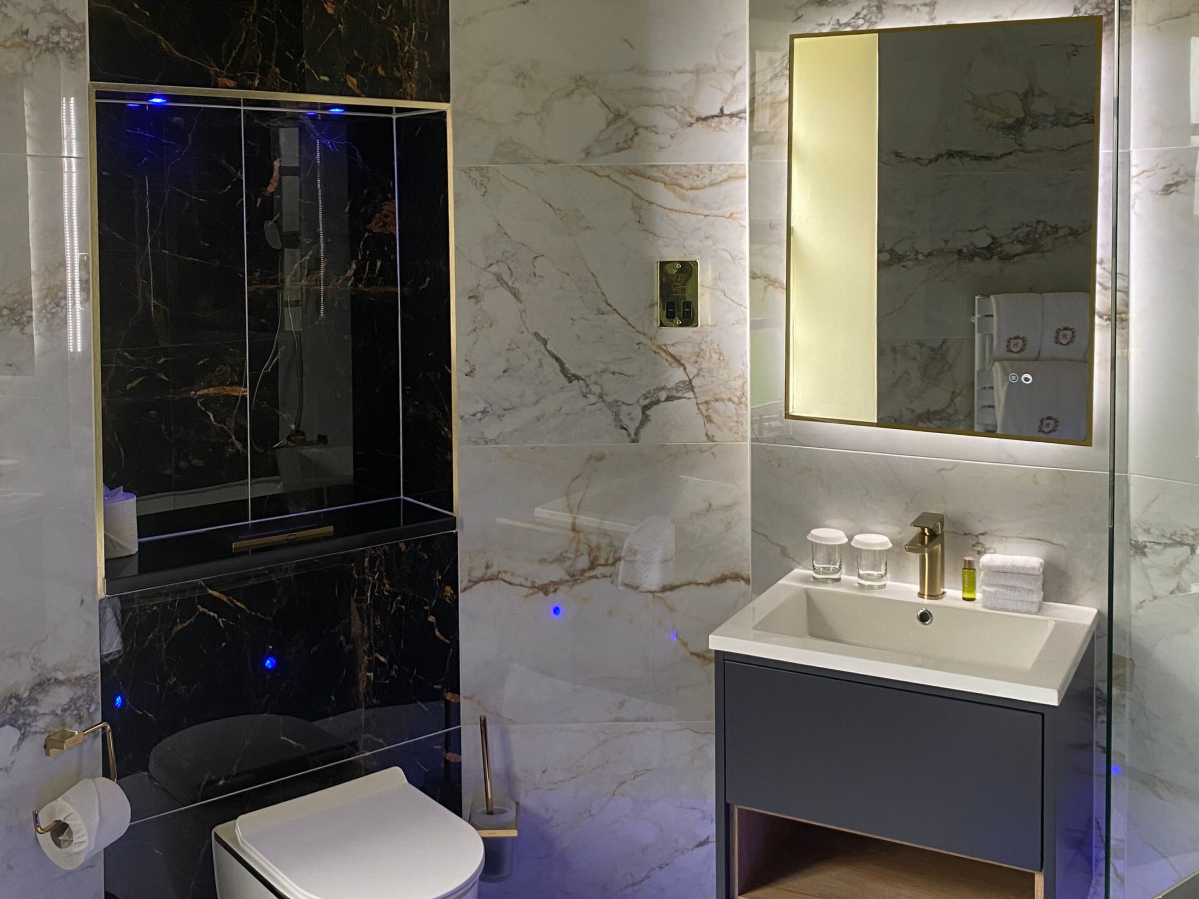 Un baño moderno con tocador de mármol, cabina de ducha con mampara de vidrio y un espejo grande.