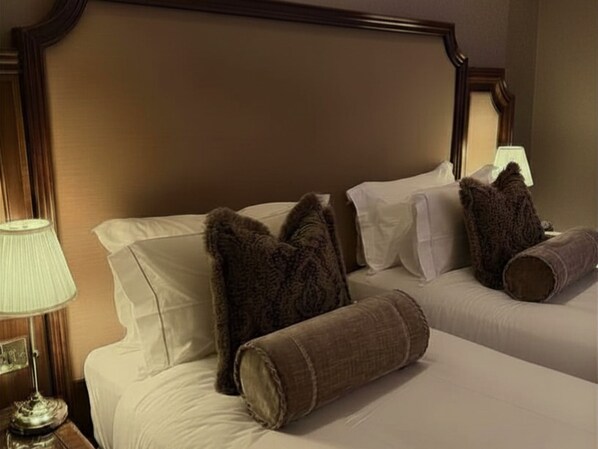 Habitación de hotel con cabecera de madera, dos camas con ropa blanca y una lámpara en la mesita de noche.