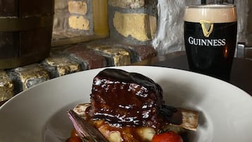 Een bord eten met een donkere geglazuurde vleesbereiding, omringd door groenten, en een glas Guinness bier.