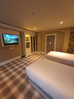 A hotel room with a television mounted on the wall, a checkered floor, a bed, and a door. - Kinnitty Castle Hotel (Kinnitty)