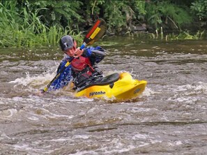 A person in a yellow kayak with 'pyranha' written on it, wearing a helmet and life jacket, navigating through a river. - Kinnitty Castle Hotel (Kinnitty)