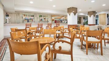 Un hall de hotel con sillas y mesas de madera, una zona de bar con diferentes botellas y un diseño de techo moderno.