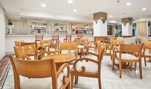 Un hall d’hôtel avec des chaises et des tables en bois, un coin bar avec différentes bouteilles et un design moderne au niveau du plafond.