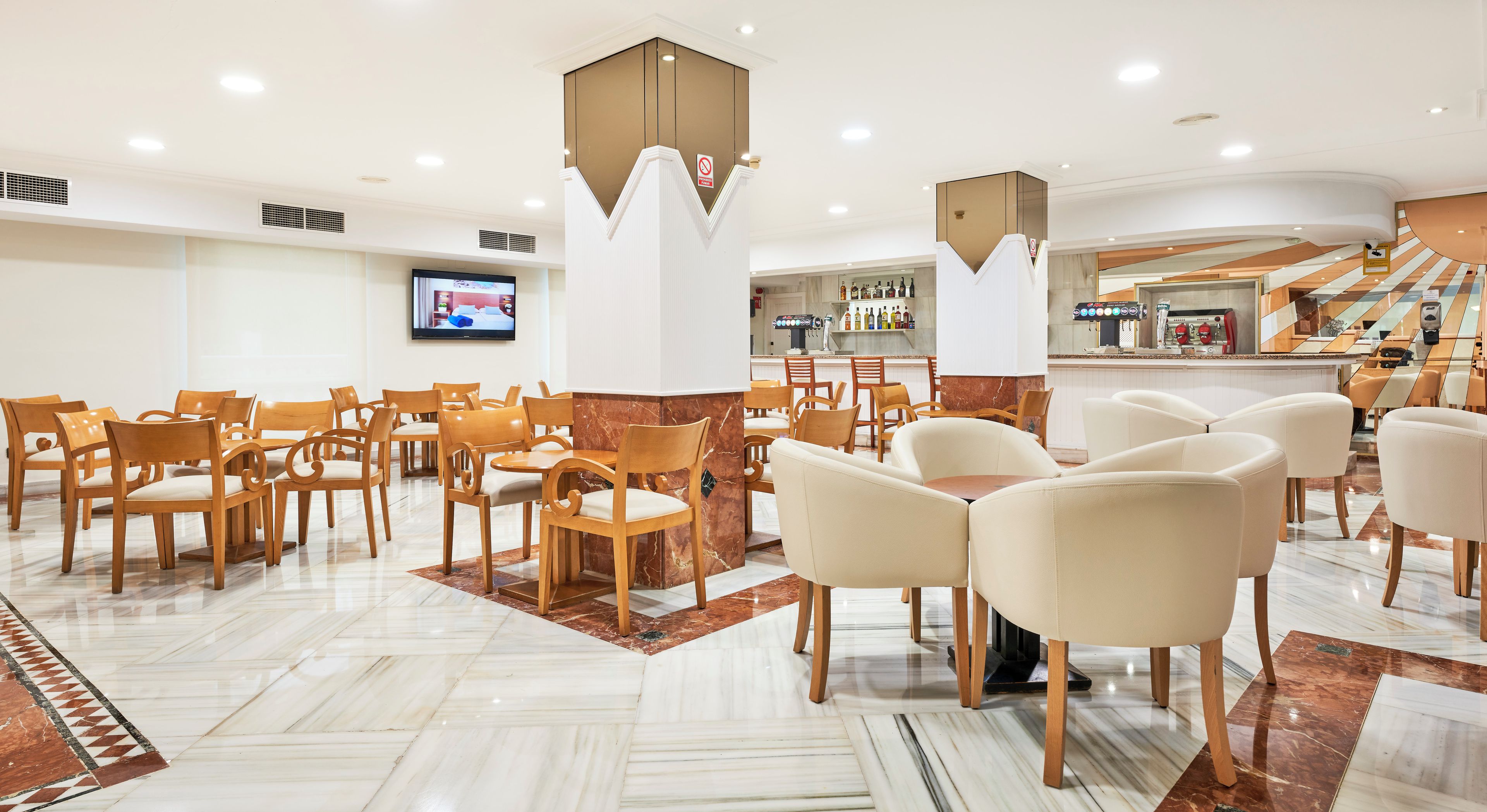 Un vestíbulo de hotel con varias zonas de estar, una pantalla de televisión y un área de bar.