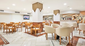 Un hall d’hôtel doté de plusieurs espaces salon, d’un écran de télévision et d’un bar.