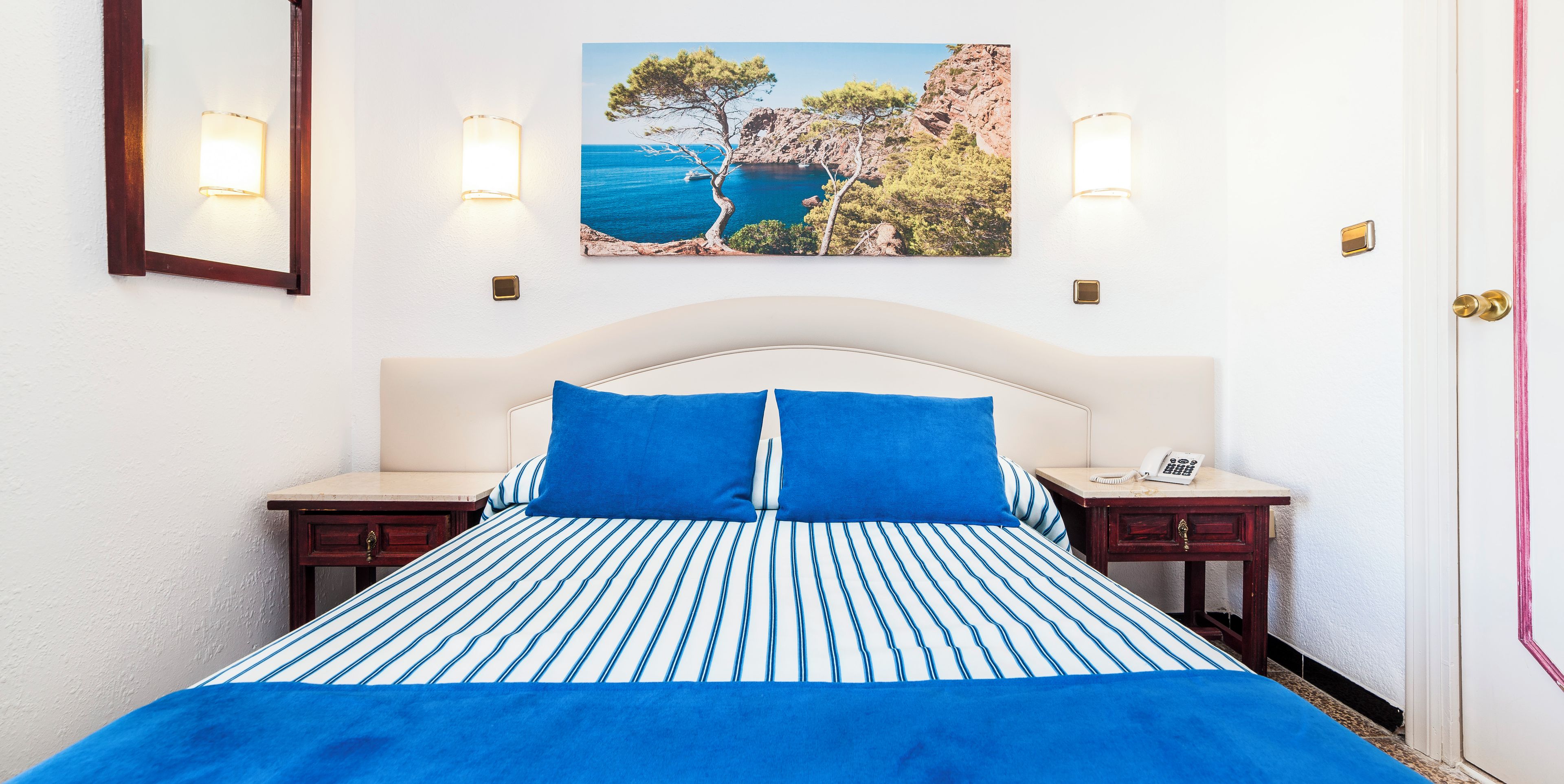 A bed with a striped blue and white bedspread, two blue pillows, and a white headboard.