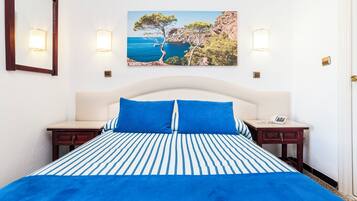 A bed with a striped blue and white bedspread, two blue pillows, and a white headboard.