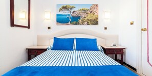 A bed with a striped blue and white bedspread, two blue pillows, and a white headboard.