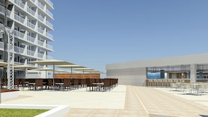 Ein moderner Innenhof eines Hotels mit Außenbestuhlung, einem Pool und einem Hochhaus mit Balkonen.
