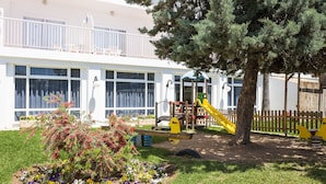 Ein Kinderspielbereich mit Rutsche und Klettergerüst, umgeben von einem Garten mit bunten Blumen und einem großen Baum.