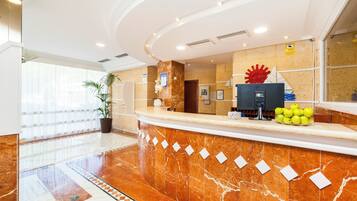 Zona de recepción de hotel con mostrador de mármol, una gran pieza decorativa roja y un frutero con manzanas.
