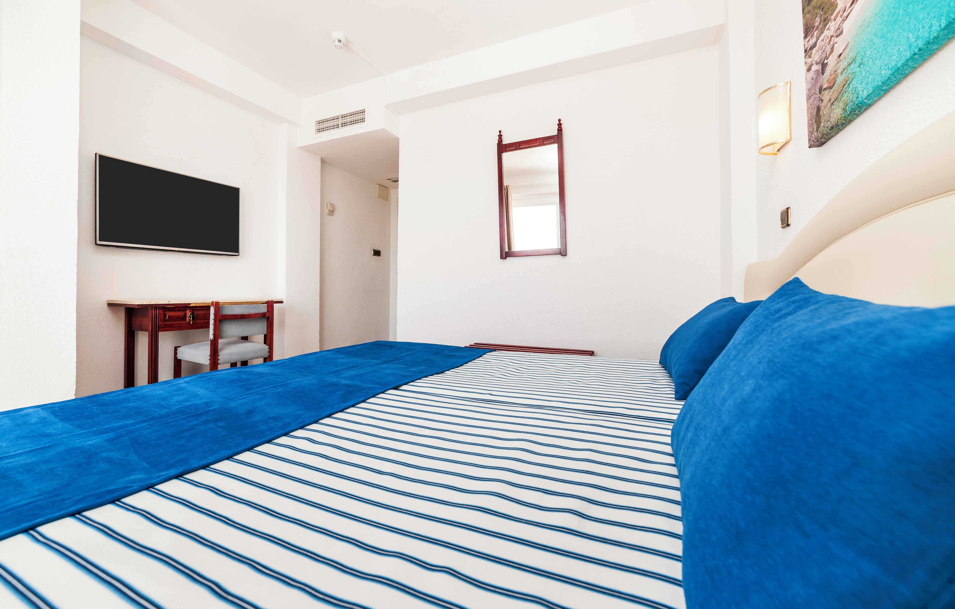 Una habitación de hotel con una cama, un televisor de pantalla plana, un escritorio y un espejo.