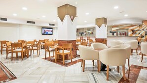 Eine Hotelhalle mit mehreren Sitzbereichen, einer Bar und einem Fernsehbildschirm.