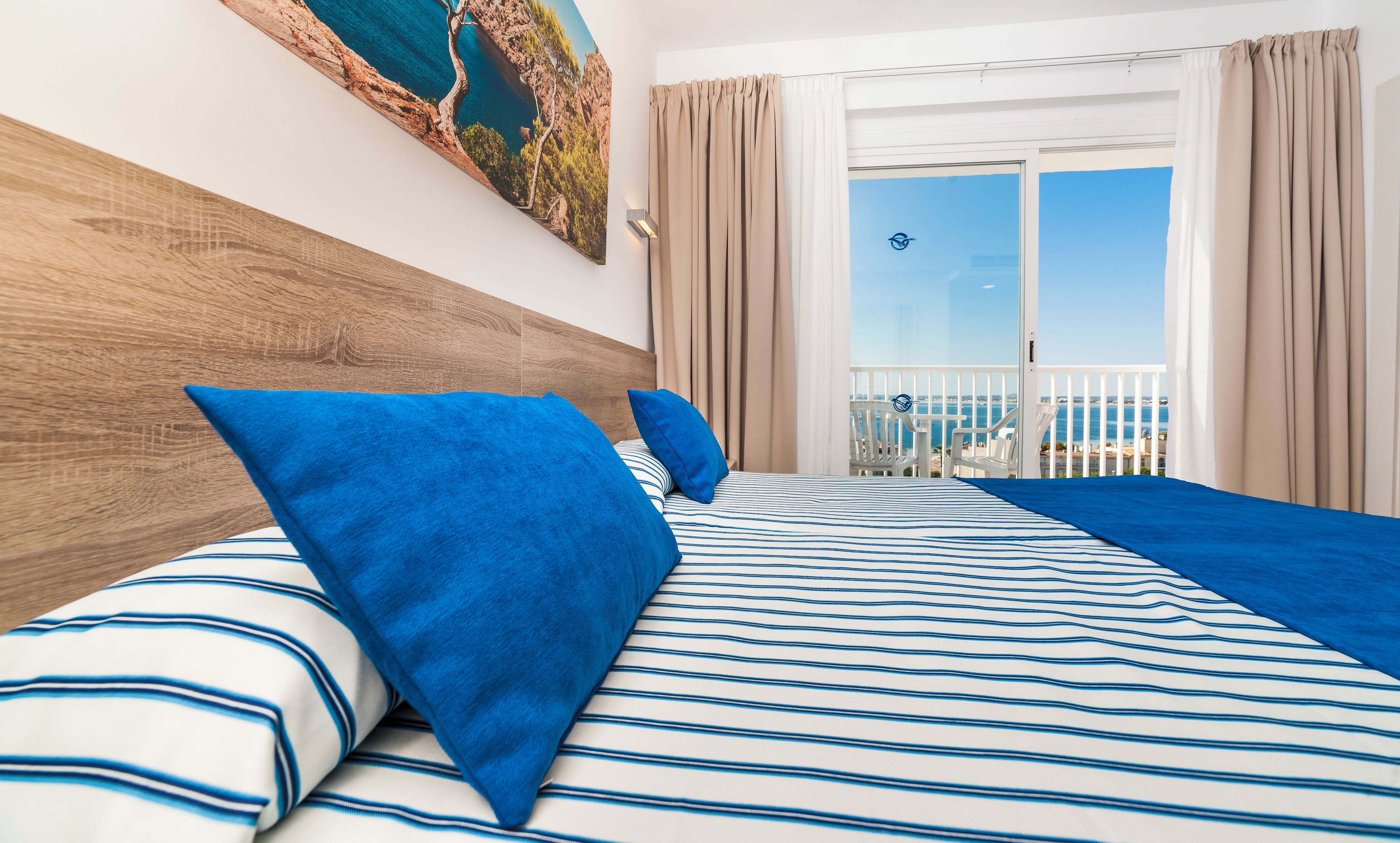 Habitación de hotel con una cama grande, cabecera de madera y balcón con vistas al mar.