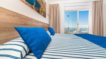 Habitación de hotel con una cama grande, cabecera de madera y balcón con vistas al mar.