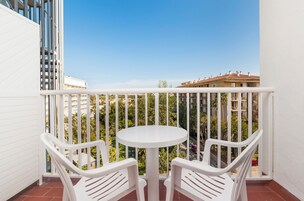 Un balcón con una mesa blanca y dos sillas blancas, con vistas a una zona residencial con edificios y vegetación.