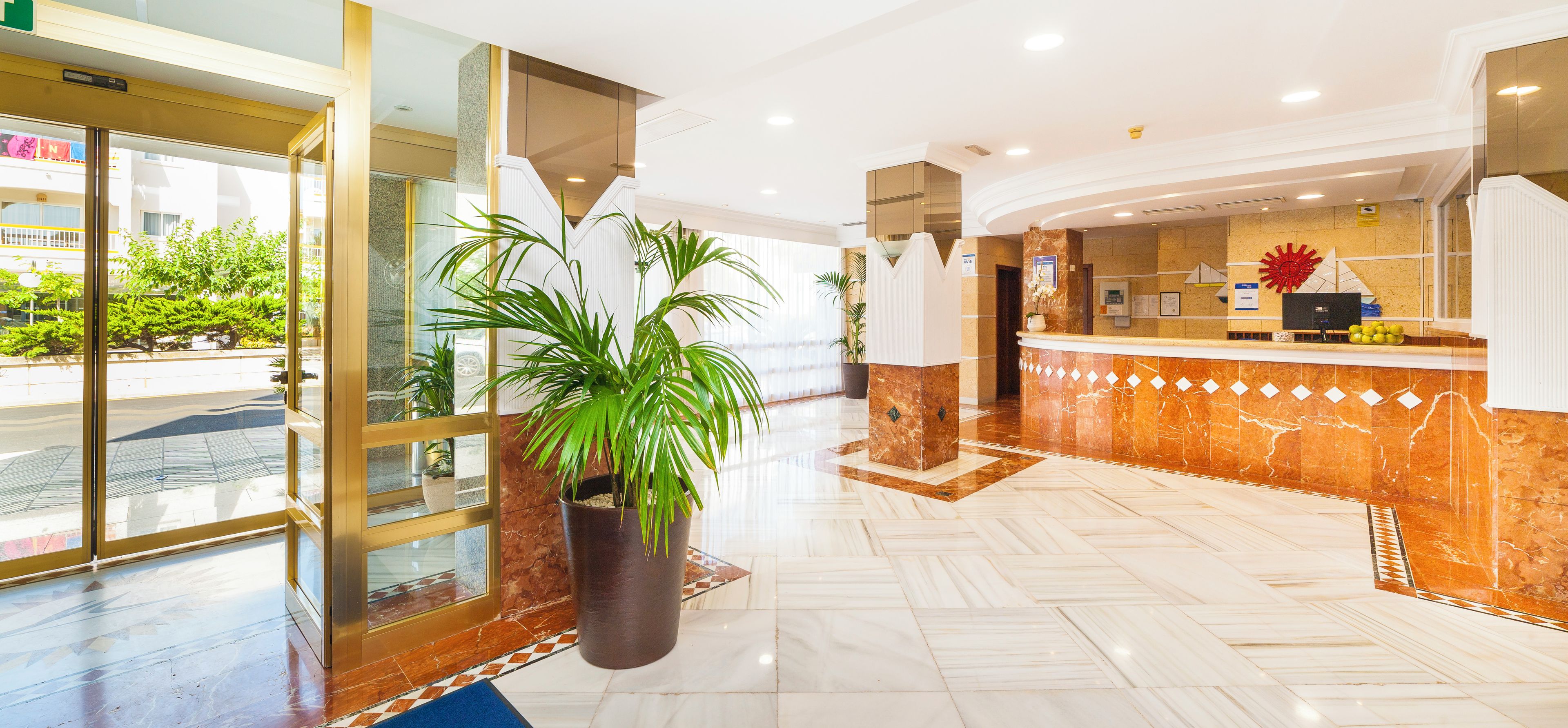 A hotel reception area with a marble floor, a reception desk, and a potted plant.