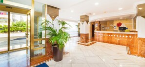 Un hall d’hôtel avec un sol en marbre, un comptoir d’accueil et une plante en pot.