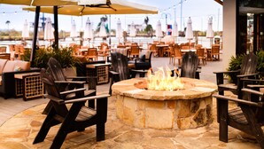 An outdoor seating area with stone fire pit, wooden chairs, and umbrellas. - Kemah Boardwalk Inn (Kemah)