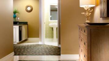A hallway with a patterned carpet, a wooden cabinet with a lamp, and a door leading to a bathroom.