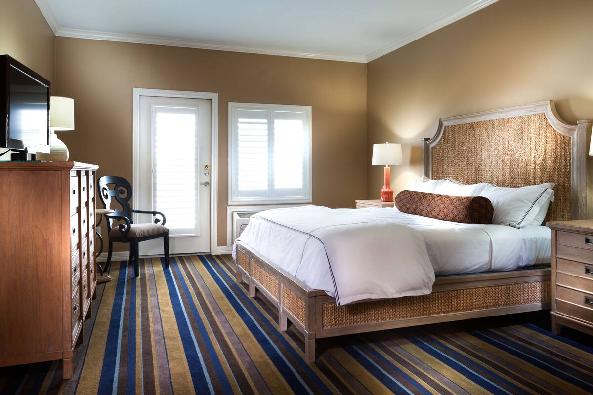 A hotel room with a large bed, a desk with a chair, a television, and two windows.