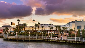 A waterfront hotel with a boardwalk, palm trees, and a sunset sky.