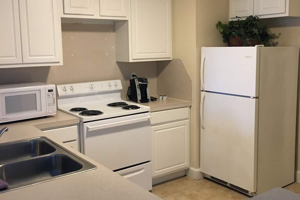 A compact kitchen with white cabinets, a stove, a microwave, a refrigerator, and a sink.