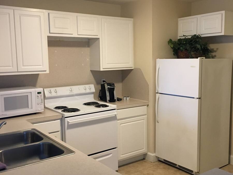 A compact kitchen with white cabinets, a stove, a microwave, a refrigerator, and a sink.
