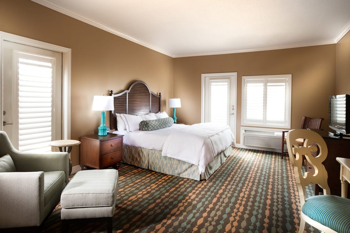 A hotel room with a bed, two bedside tables with lamps, a chair, a television, and a patterned carpet.